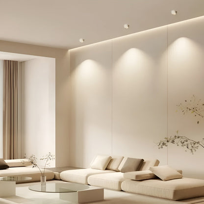 Drei weiße Einbaustrahler an der Decke eines hellen Wohnzimmers beleuchten die Wand über einem beigen Sofa 2