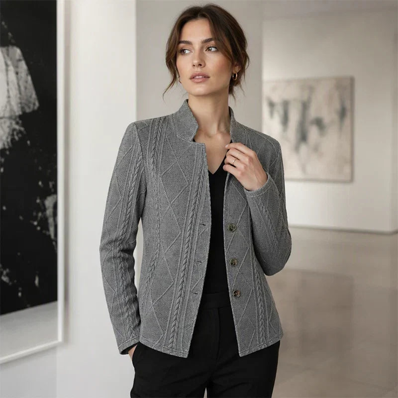 Grauer strukturierter Blazer mit Knopfleiste, kombiniert mit schwarzem V-Ausschnitt-Top und schwarzer Hose in einer hellen Galerie. 11