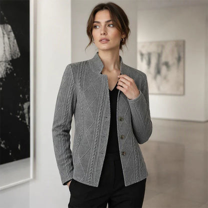 Grauer strukturierter Blazer mit Knopfleiste, kombiniert mit schwarzem V-Ausschnitt-Top und schwarzer Hose in einer hellen Galerie. 11