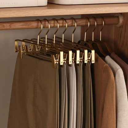 Mehrere goldene Hosenbügel mit Clips hängen an einer Holzstange im Schrank, daran beige und braune Hosen 3