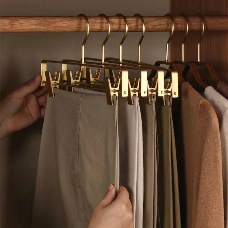 Hand zieht eine Hose aus einer Reihe goldener Clip-Bügel an einer Holzstange im Kleiderschrank 7