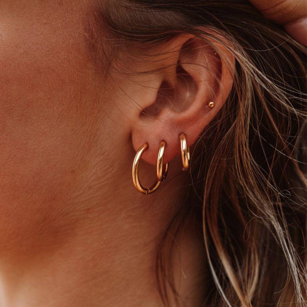 Goldene Mini-Creolen-Ohrringe am Ohr einer Frau, modischer Schmuck, Nahaufnahme.