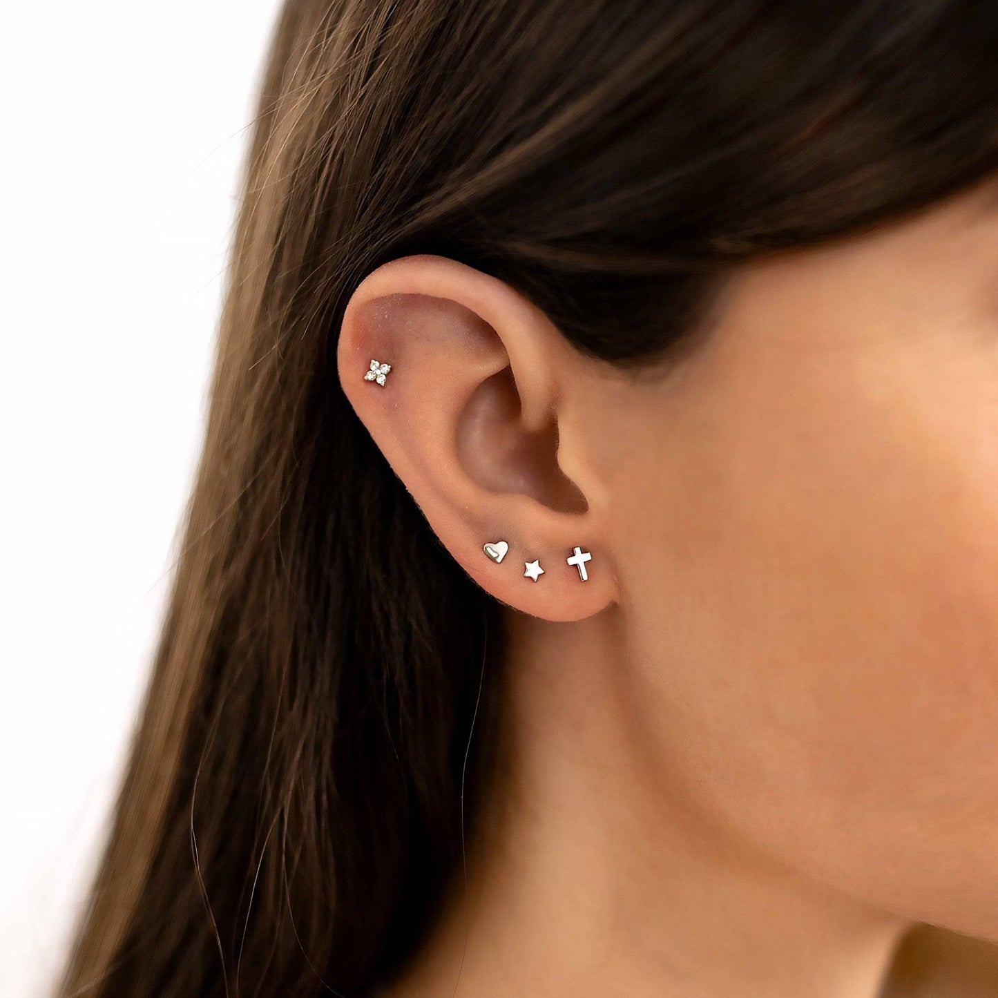 Frau mit silbernen Mini-Sterne-Ohrringen, Herz- und Kreuz-Design, modischer Schmuck.