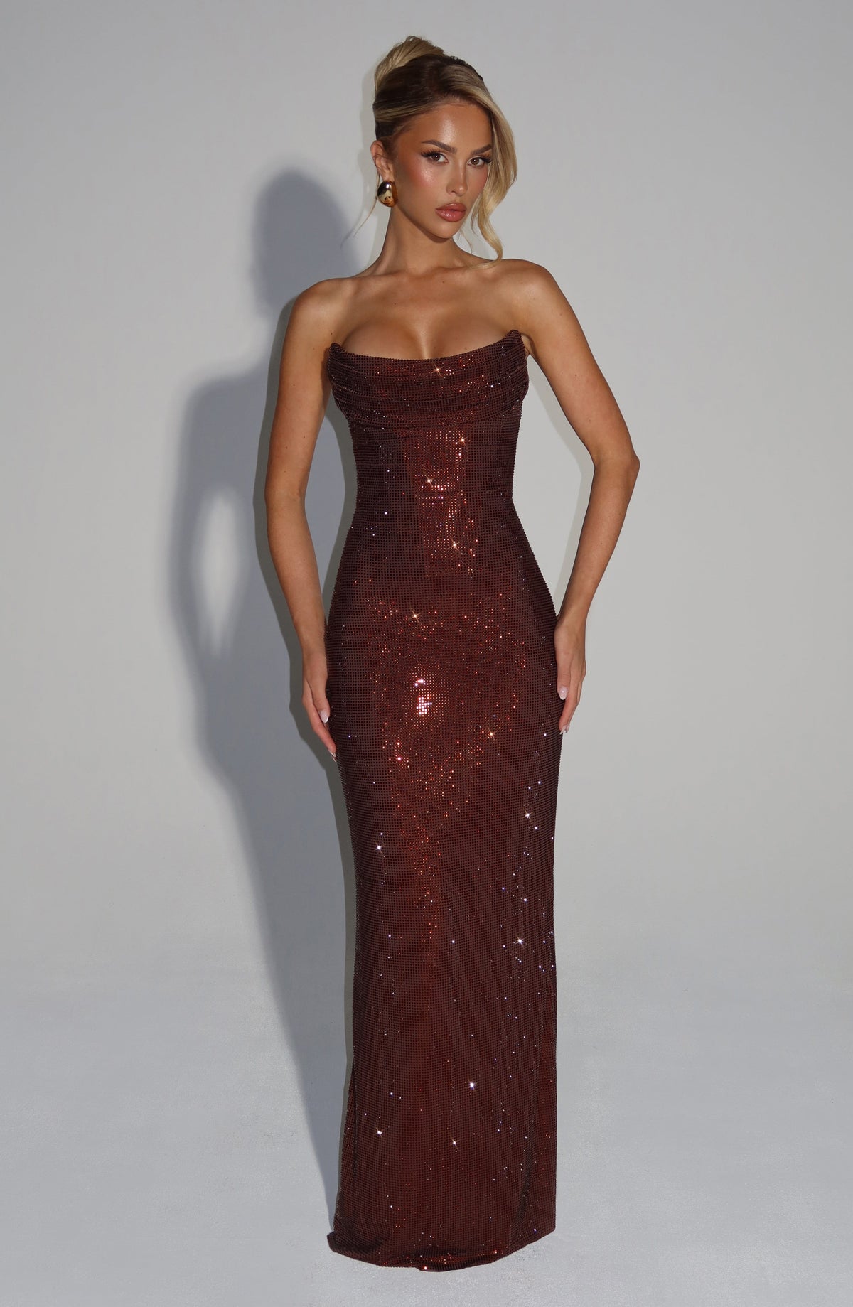 Model in dunkelbraunem Strass-Maxikleid, trägerlos mit drapiertem Mieder, frontal vor hellem Hintergrund fotografiert. 5