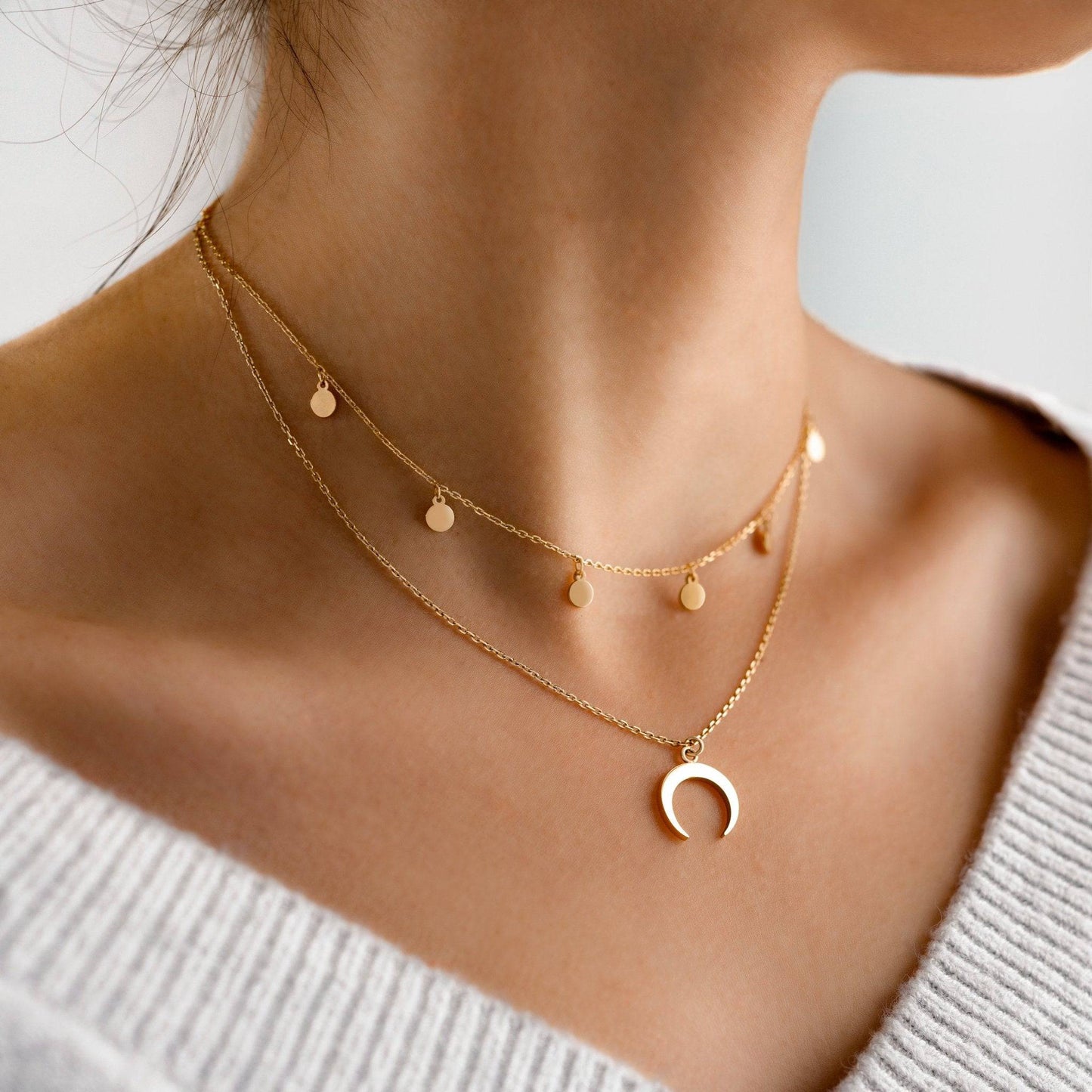 Frau trägt goldene Halskette mit Halbmond-Anhänger und kleinen runden Anhängern, eleganter Schmuck.