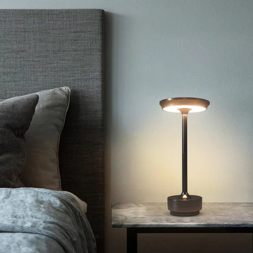 Moderne Nachttischlampe, schwarz, LED, auf Marmortisch neben grauem Bett, Schlafzimmerbeleuchtung.