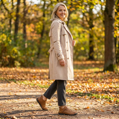 Frau im beigen Trenchcoat geht auf einem Waldweg im Herbstlaub und trägt braune Sneaker, Seitenansicht. 18