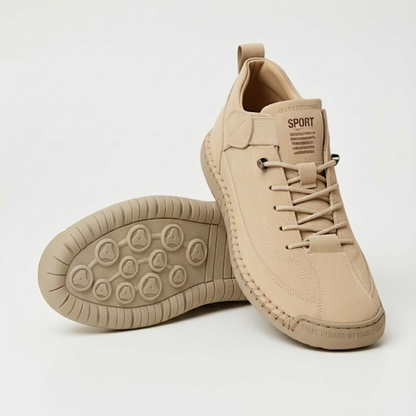 Beiger Sneaker aus Veloursleder-Optik mit Schnürung, daneben ein zweiter Schuh mit der profilierten Laufsohle nach oben, heller Hintergrund. 1