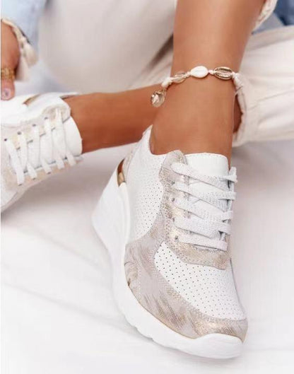Weiße Damen-Sneaker mit Keilabsatz, goldenen Akzenten und Muschelarmband.