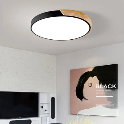 Schwarze runde Deckenleuchte mit Holzsegment an der Decke eines Wohnzimmers, darunter Fernseher und ein Wandbild. 1