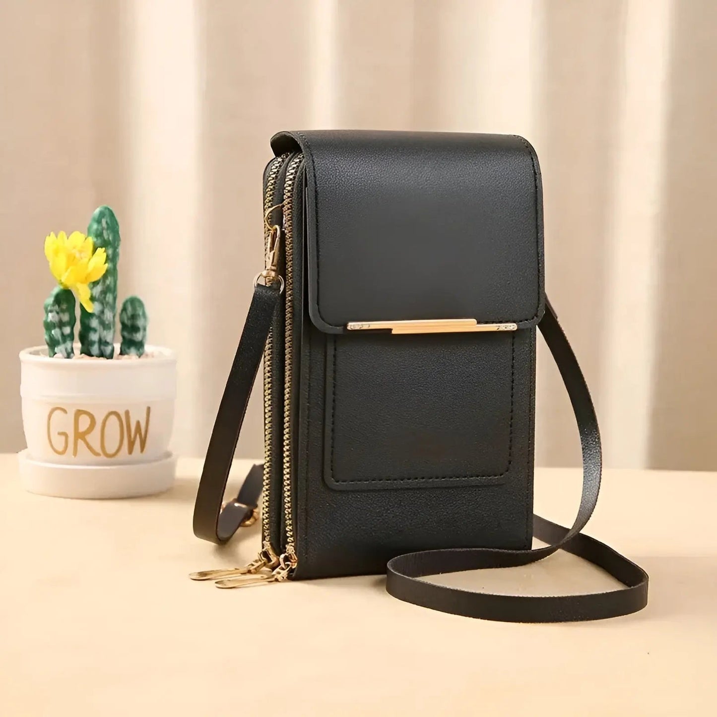 Schwarze Lederhandtasche mit Schulterriemen, goldenen Reißverschlüssen, neben Kaktus im Topf.