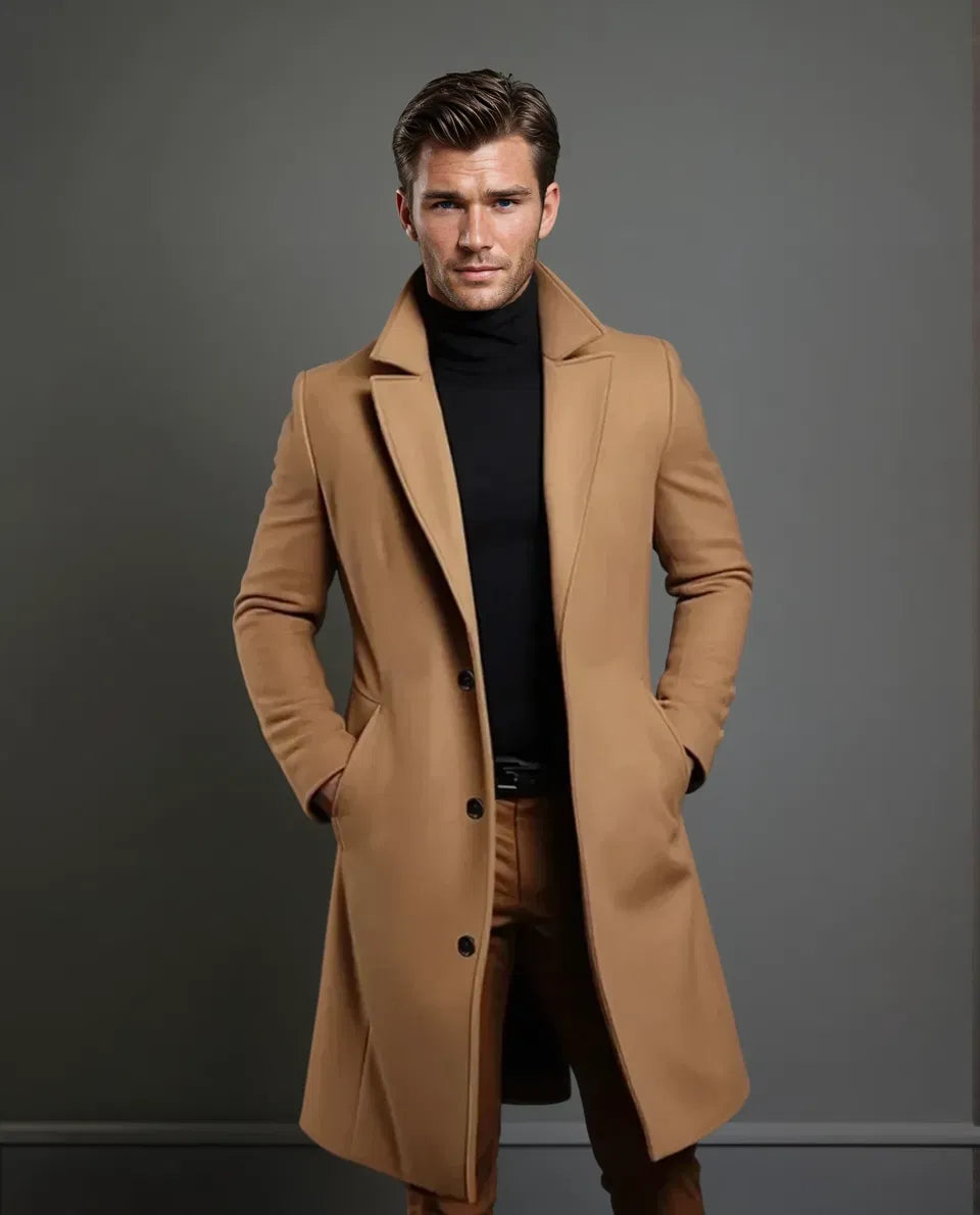 Ganzkörperansicht des kamelbraunen Mantels an einem Model mit Gesicht, Hände in den Taschen, dazu schwarzer Rollkragenpullover und braune Hose. 5