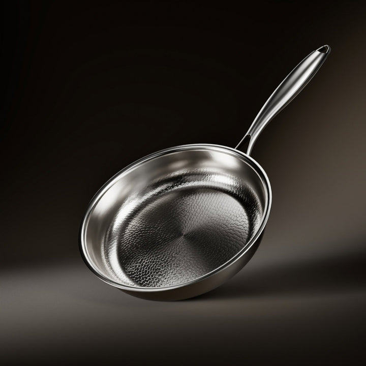 Schräg gestellte Pfanne mit gehämmerter Innenfläche und langem Metallgriff vor dunklem Hintergrund, von oben in die Pfanne gesehen. 1