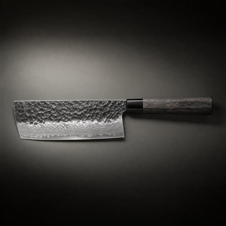 Seitenansicht des Messers waagerecht vor dunklem Hintergrund, die breite Klinge mit gehämmerter Oberfläche und Schichtstahlmuster neben dem dunklen Holzgriff. 2