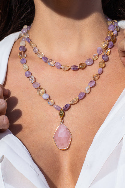 Frau mit zweireihiger Halskette aus lila und goldenen Edelsteinen, rosa Anhänger, weißes Hemd.
