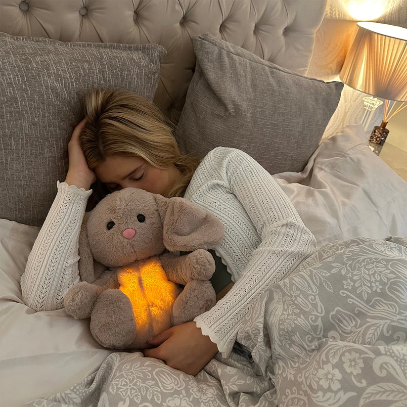 Schlafende Frau mit hellen Haaren im Bett, den Plüschhasen mit leuchtendem Bauch fest im Arm. 16