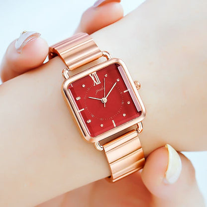 Roségoldene Armbanduhr mit rotem Zifferblatt, quadratischem Gehäuse und Metallarmband.