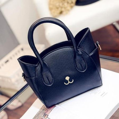 Schwarze Lederhandtasche mit goldfarbenem Logo auf Glastisch, elegant und modern.