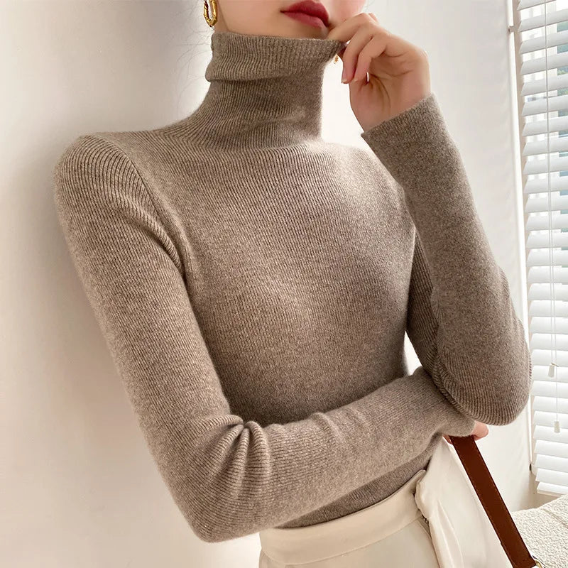 Rollkragenpullover in Taupe am Model, kombiniert mit heller Hose, die Hand am Kragen 6