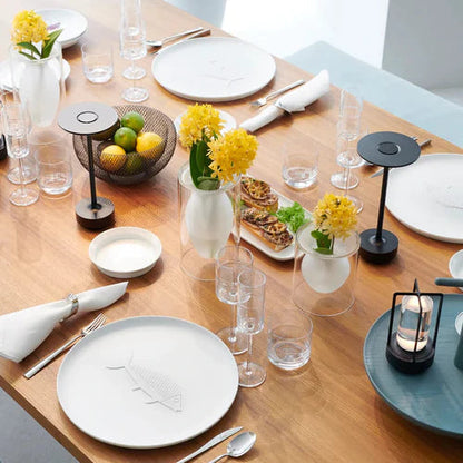 Esstisch mit gelben Blumen, modernen Lampen, Obstschale und Geschirr, elegantes Restaurantambiente.