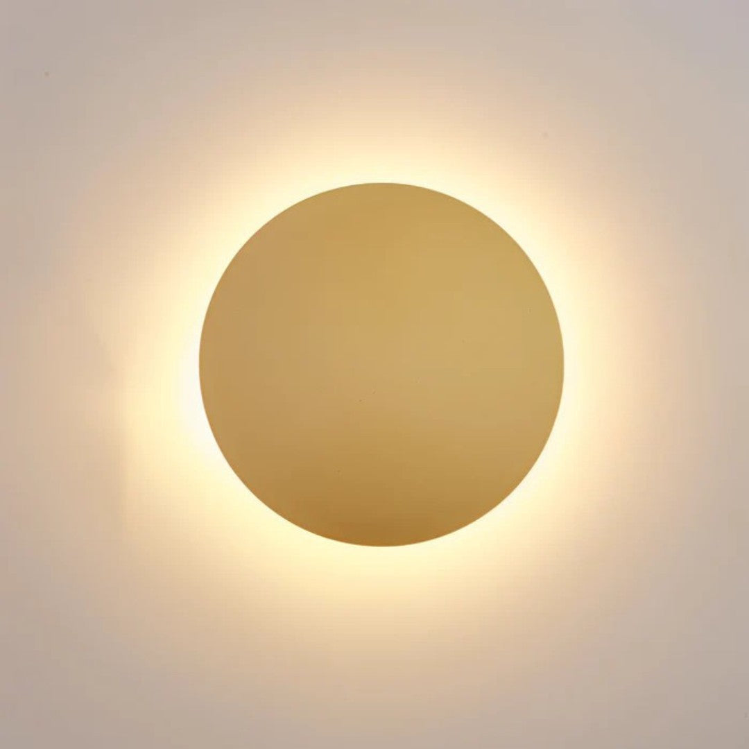 Goldfarbene Wandleuchte in Nahaufnahme, hinter der Scheibe strahlt ein warmweißer Lichtkranz 1