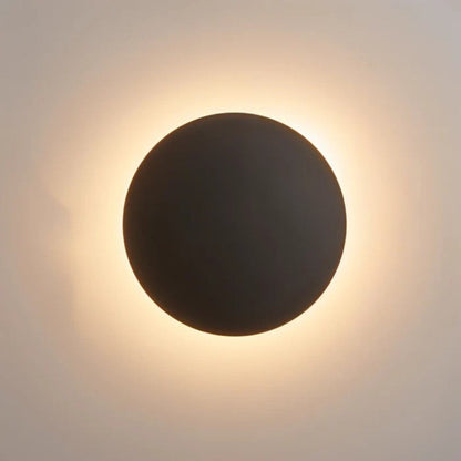Schwarze Variante der runden Wandleuchte in Nahaufnahme mit warmweißem Leuchtring an der Wand 2