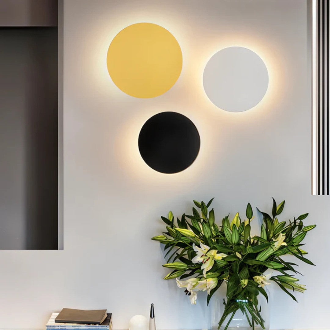 Drei Wandleuchten in Gold, Weiß und Schwarz an einer Wand über einer Blumenvase 4