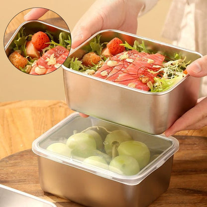 Hände halten eine Edelstahlbox mit Salat und rohem Lachs über einer Box mit durchsichtigem Deckel und Trauben, kleines Detailbild oben links. 1