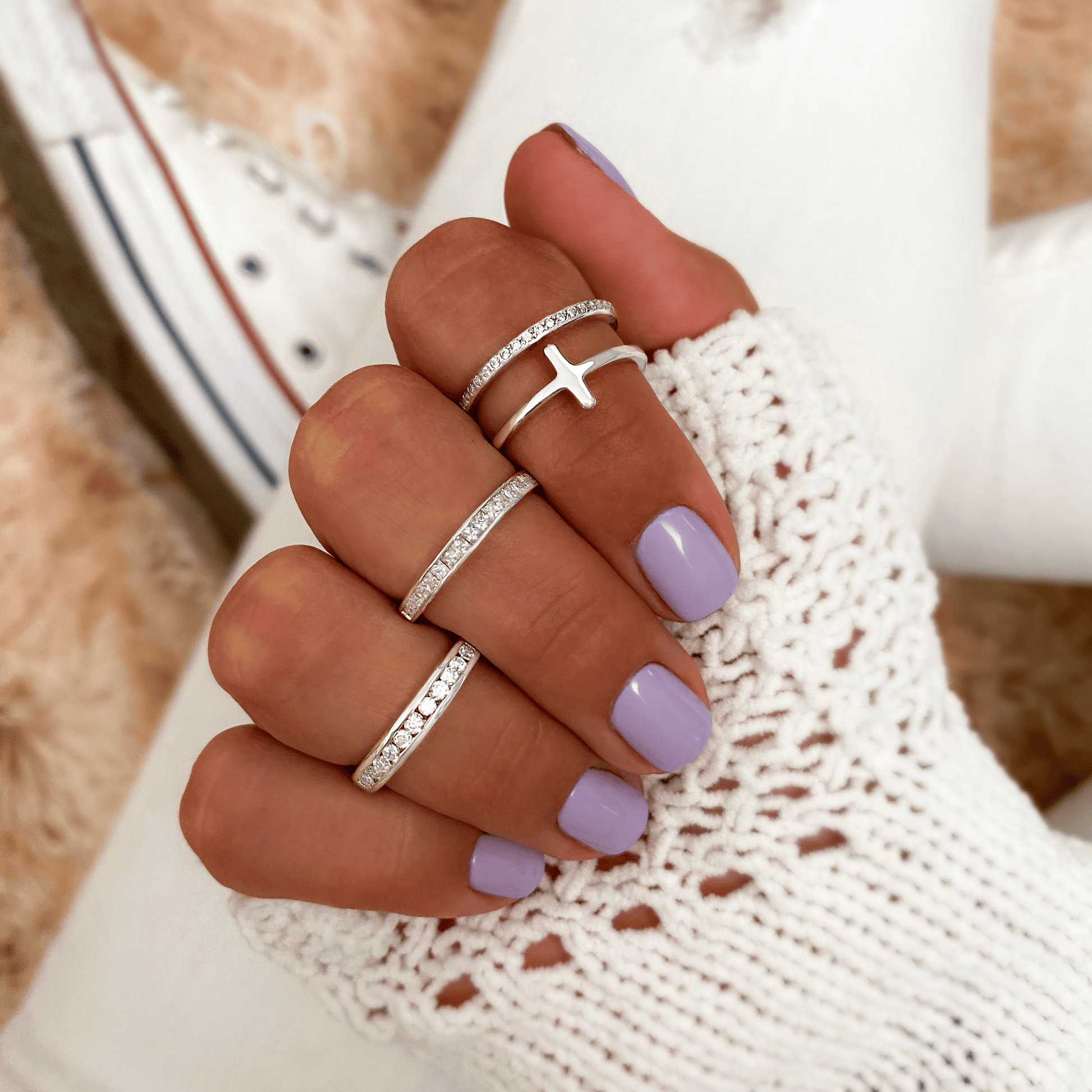 Frau mit lila Nagellack trägt silberne Ringe, Kreuzdesign, gestrickter weißer Pullover.