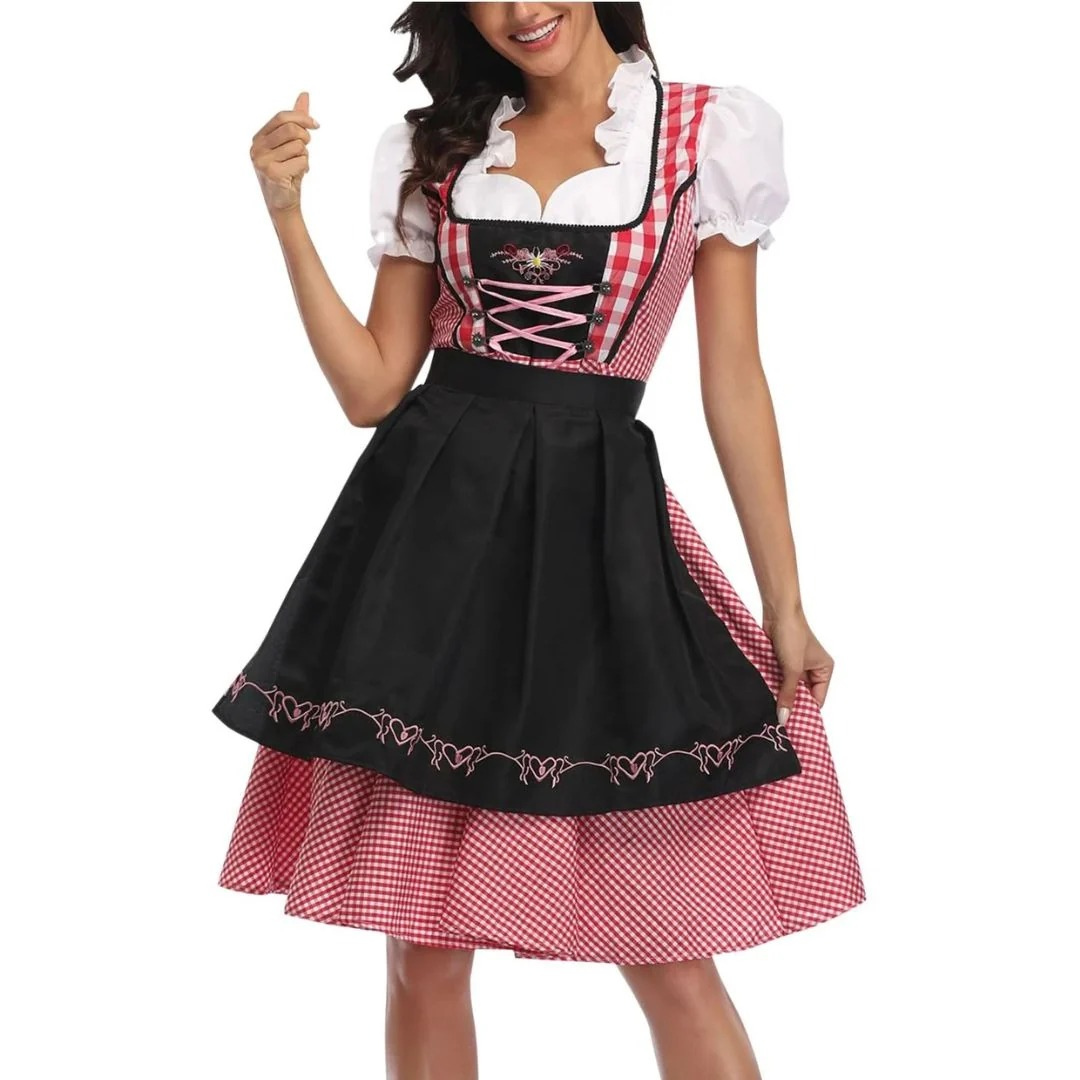 Frau im rot-weiß karierten Dirndl mit schwarzer, bestickter Schürze, rosa Schnürung und weißer Puffärmelbluse, frontal im Halbbild. 1