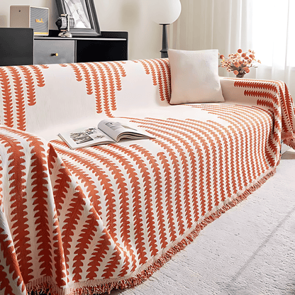 Sofaüberwurf in orange-weißem Blattmuster mit Fransenkante, im selben Wohnzimmer mit weißem Kissen und Zeitschrift. 7