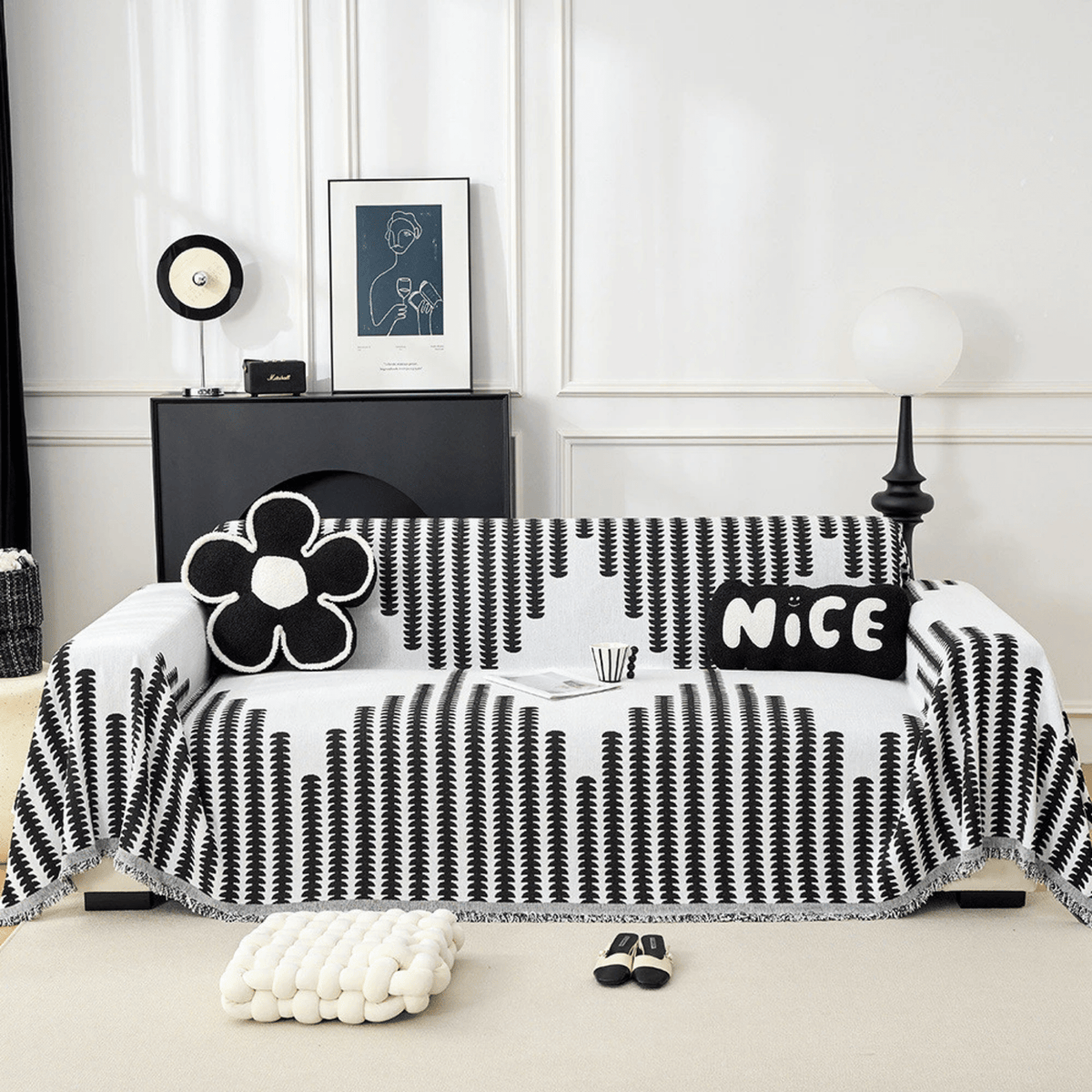 Sofa frontal mit schwarz-weiß gemustertem Überwurf mit Fransenkante, dekoriert mit Blumenkissen, im hellen Wohnzimmer mit schwarzem Sideboard. 1