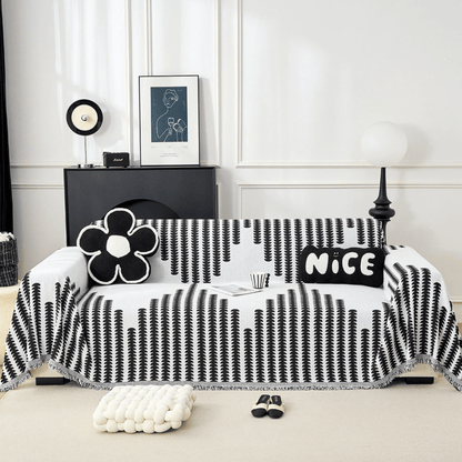 Sofa frontal mit schwarz-weiß gemustertem Überwurf mit Fransenkante, dekoriert mit Blumenkissen, im hellen Wohnzimmer mit schwarzem Sideboard. 1