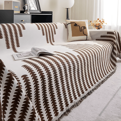 Sofaüberwurf in braun-weißem Muster mit Fransenkante, kombiniert mit einem Kissen mit abstrakter Linienzeichnung. 9
