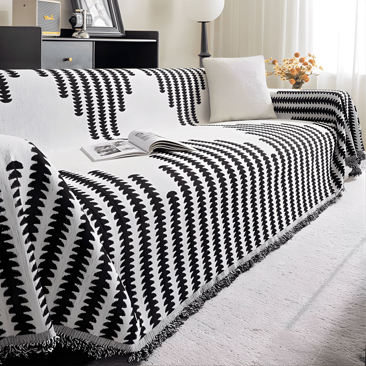 Sofa mit schwarz-weißem Überwurf und Fransen von der Seite, ein weißes Kissen und aufgeschlagene Zeitschrift auf dem Sitz. 6