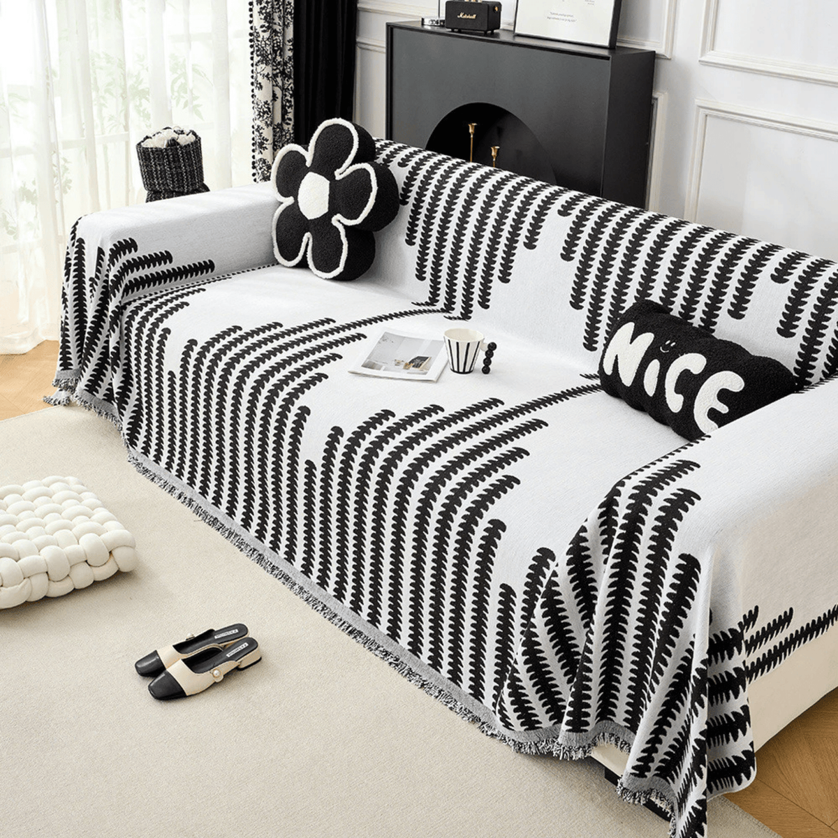 Schräger Blick auf das Sofa mit schwarz-weißem Überwurf, Blumenkissen, Kissen mit Schriftzug, Tasse und Zeitschrift auf der Sitzfläche. 5