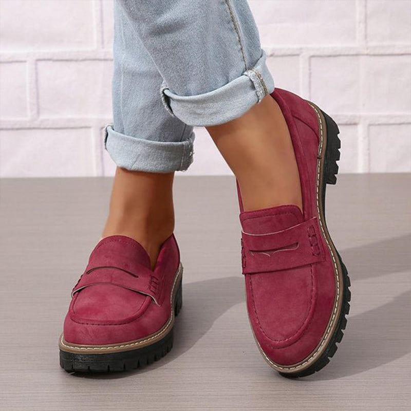 Weinrote Loafer mit Zierlasche an den Füßen einer Trägerin in hellblauer, umgekrempelter Jeans vor weißer Wand. 4