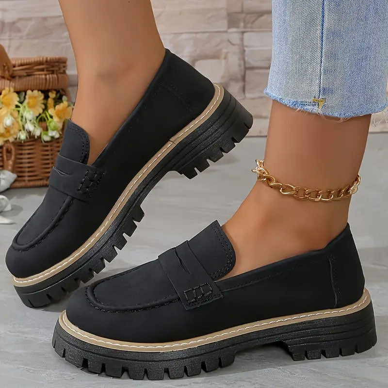 Schwarze Loafer mit Plateausohle und heller Zierkante an den Füßen, dazu goldene Fußkette und Jeans. 12