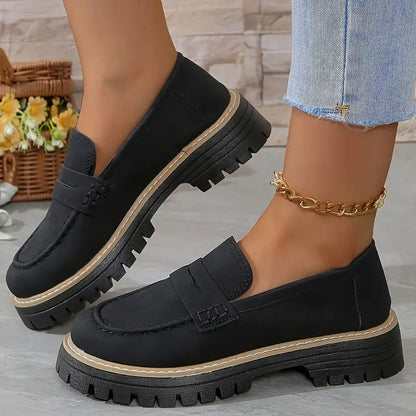 Schwarze Loafer mit Plateausohle und heller Zierkante an den Füßen, dazu goldene Fußkette und Jeans. 12