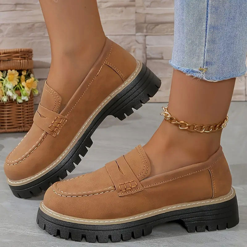 Hellbraune Loafer mit orangefarbener Kontrastnaht und dicker Profilsohle an den Füßen, mit goldener Fußkette. 17