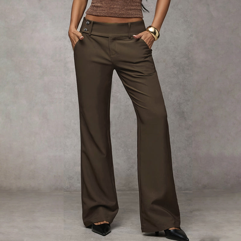 Frontansicht der braunen Hose mit breitem Bund und zwei Knöpfen seitlich, Model mit Händen in den Taschen. 3