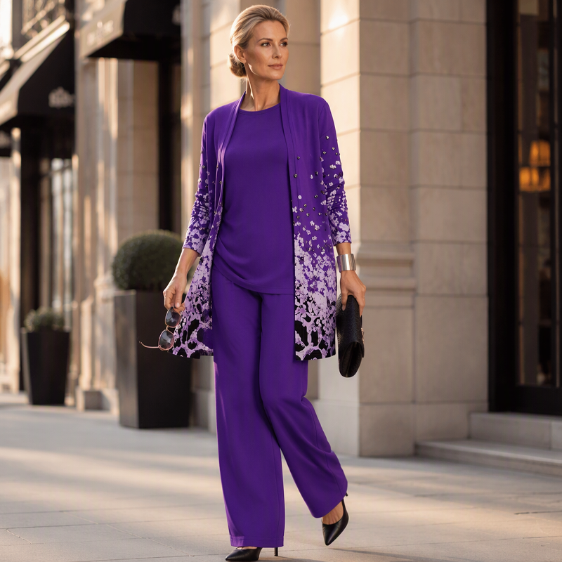 Model in violettem Set mit gemustertem Cardigan, weiter Hose und schwarzen Pumps, mit Clutch und Sonnenbrille auf einer Straße. 12