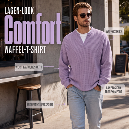 Mann mit Sonnenbrille geht in fliederfarbenem Waffelstrick-Oberteil mit V-Ausschnitt und weißem Shirt darunter an einem Café vorbei, Hände in den Hosentaschen. 1