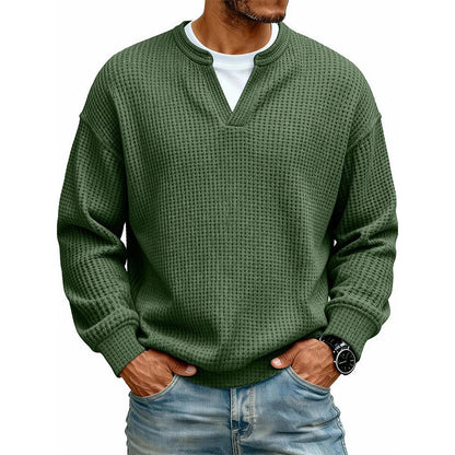 Frontansicht des Oberteils in Dunkelgrün am Model, mit weißem Shirt unter dem V-Ausschnitt, Hände in den Jeanstaschen. 18