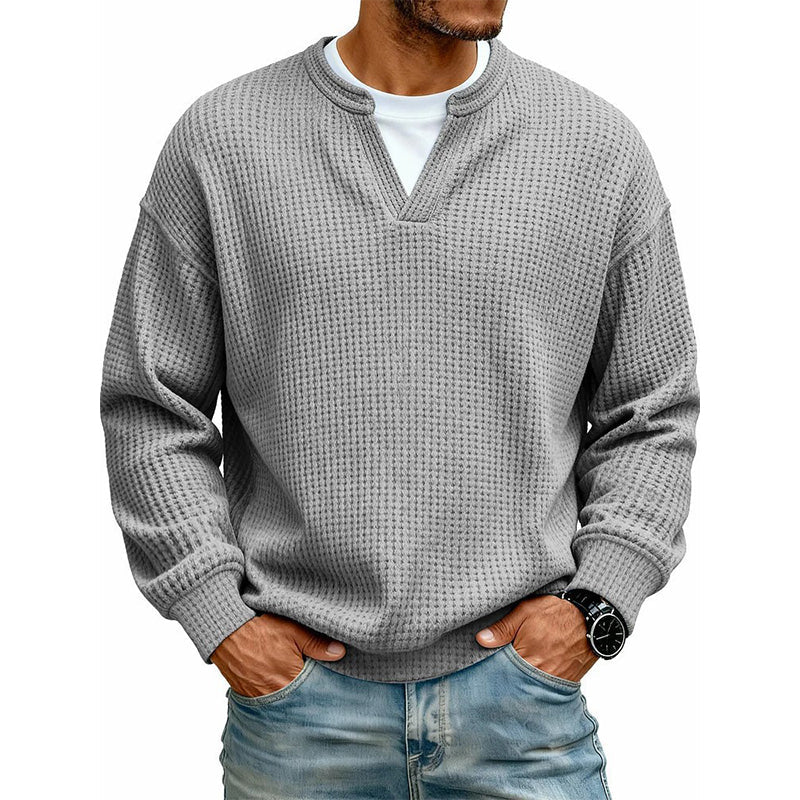 Frontansicht des Oberteils in Mittelgrau am Model, mit weißem Shirt unter dem V-Ausschnitt, Hände in den Jeanstaschen. 17