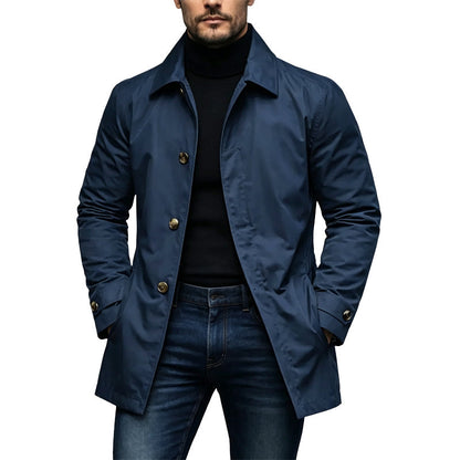 Mantel in Marineblau am Model, offen über schwarzem Rollkragenpullover getragen, mit goldfarbenen Knöpfen und Ärmelriegeln. 4