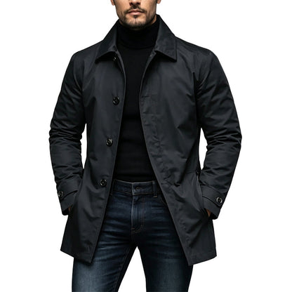 Mann trägt den Mantel in Schwarz offen über schwarzem Rollkragenpullover und Jeans, Hände in den Taschen, Frontansicht mit Knopfleiste. 1