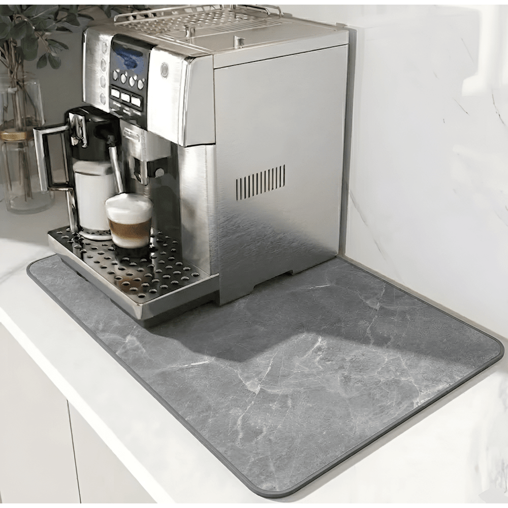 Graue Unterlage mit Marmormuster und dunklerem Rand unter einem Kaffeevollautomaten auf weißer Arbeitsplatte, links eine Pflanze in Glasvase. 12