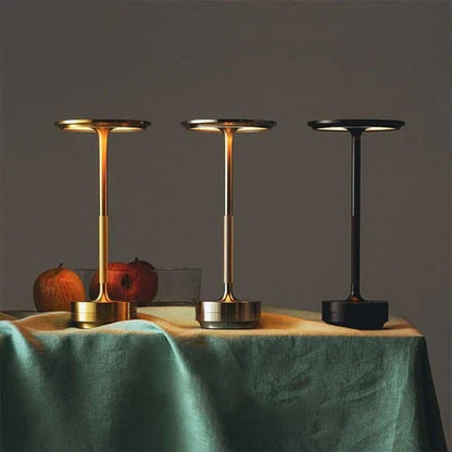 Drei moderne Tischleuchten in Gold, Silber und Schwarz auf einem Tisch mit grüner Tischdecke.