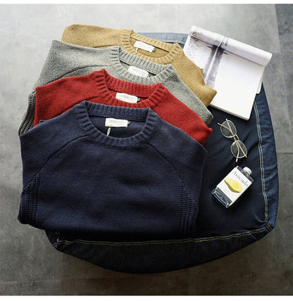 Vier gefaltete Pullover in Blau, Rot, Grau, Beige auf Tisch mit Brille und Buch.